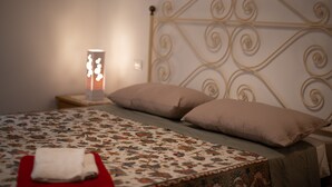 Ein ordentlich bezogenes Bett mit floralem Überwurf, zwei Kissen und einem Nachttisch mit Lampe.