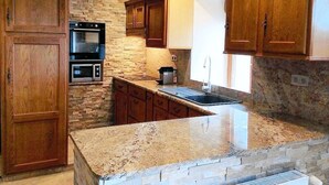 A kitchen with wooden cabinets, a stone backsplash, granite countertops, and built-in appliances including a microwave and oven.