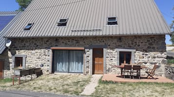 A stone house with a sloped roof, a wooden door, and a patio with outdoor furniture.