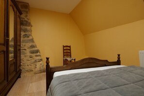 Une chambre avec un mur en pierre, un lit en bois et une chaise.
