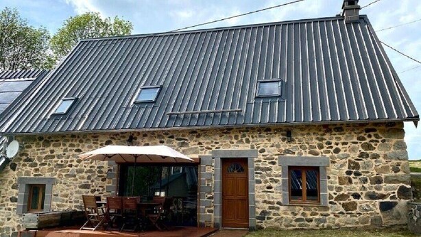 A stone building with a sloped metal roof, a wooden door, and a patio with outdoor furniture.