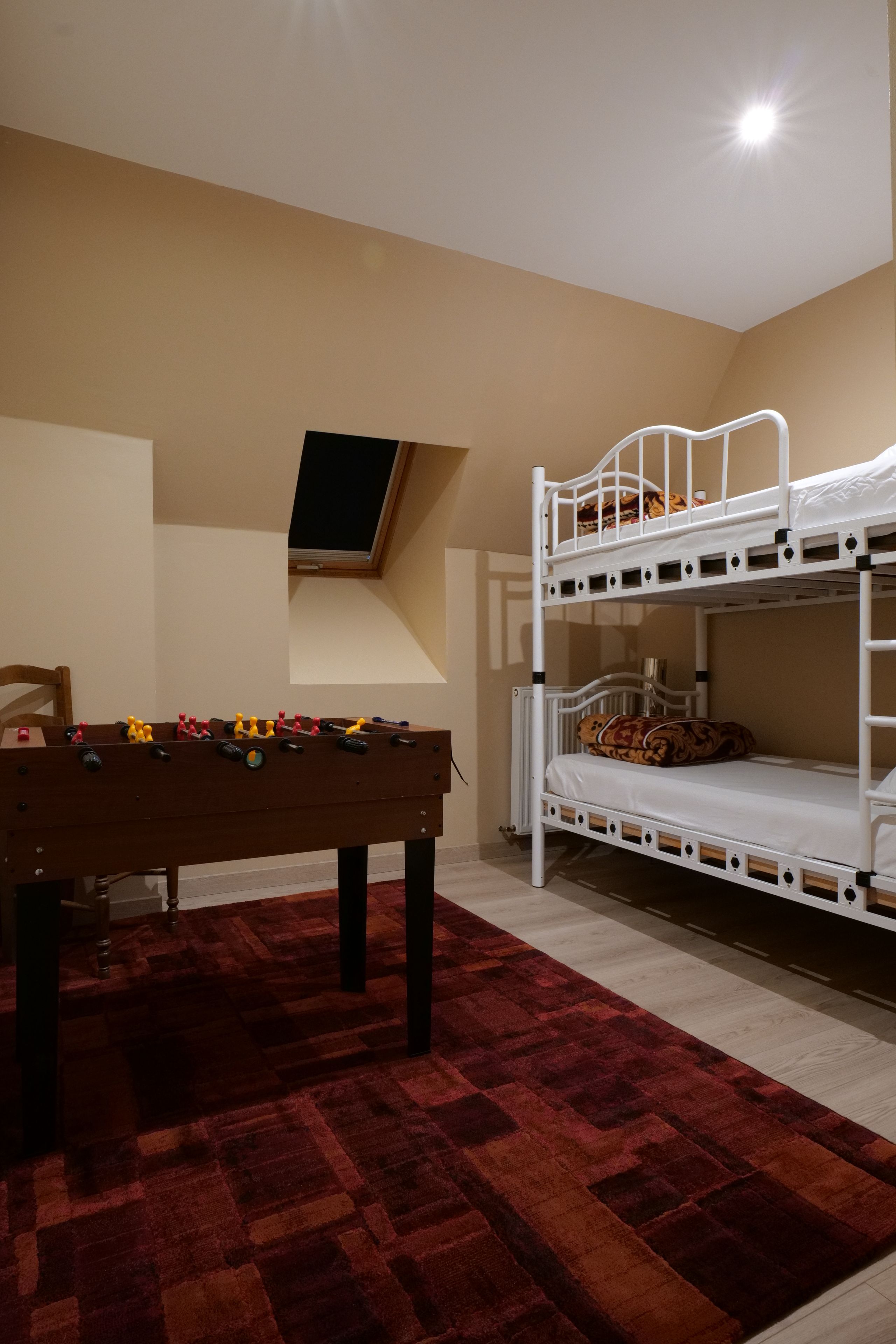Une chambre avec des lits superposés, un baby-foot et une fenêtre.