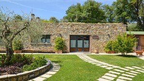 Un bâtiment en pierre avec une entrée pavée, entouré d’une pelouse bien entretenue et de plantes en pot.