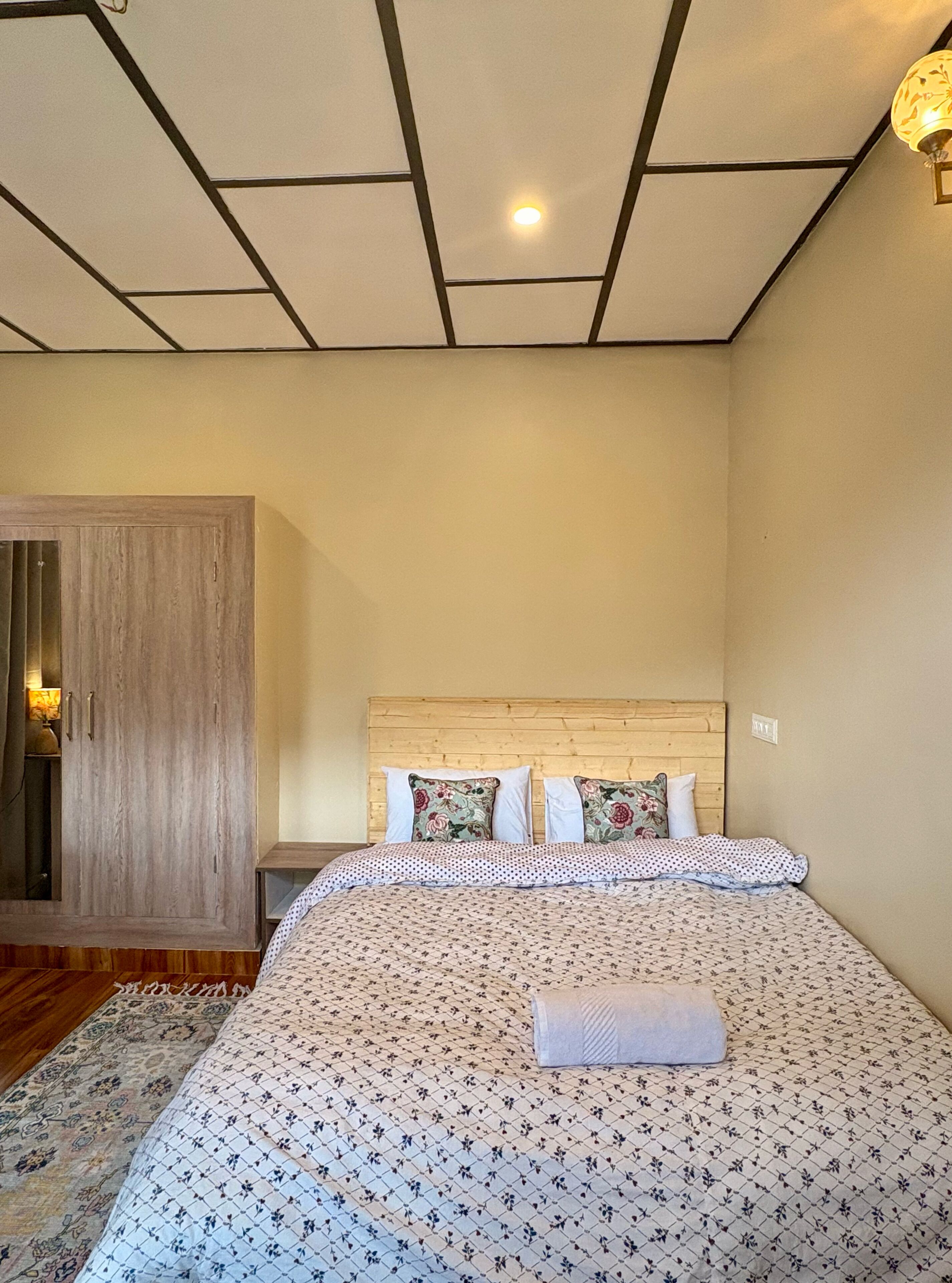 A bedroom with a wooden headboard, a bed with floral bedding, a nightstand, and a wardrobe.