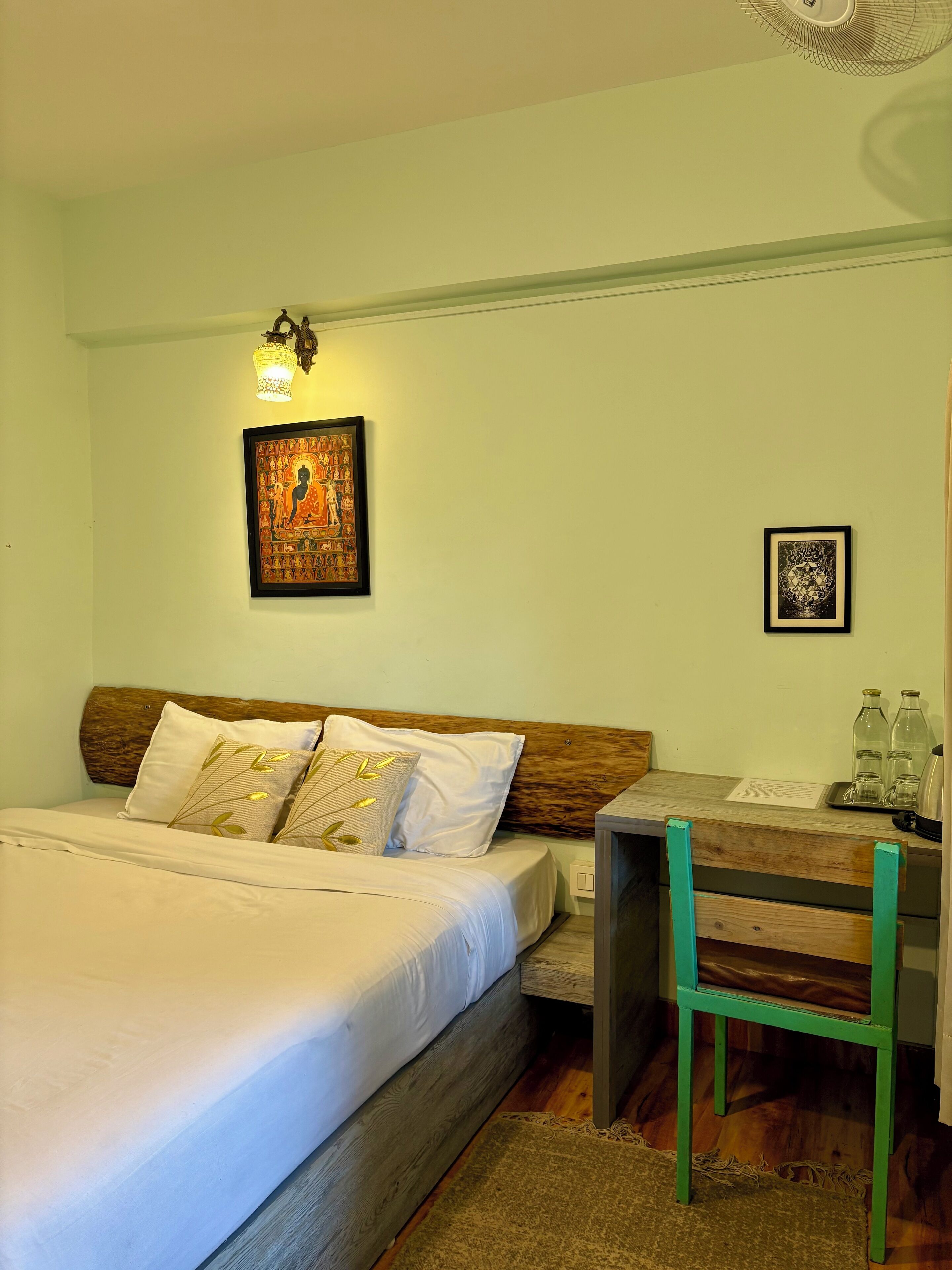A bedroom with a bed, a desk, and two framed artworks on the wall.