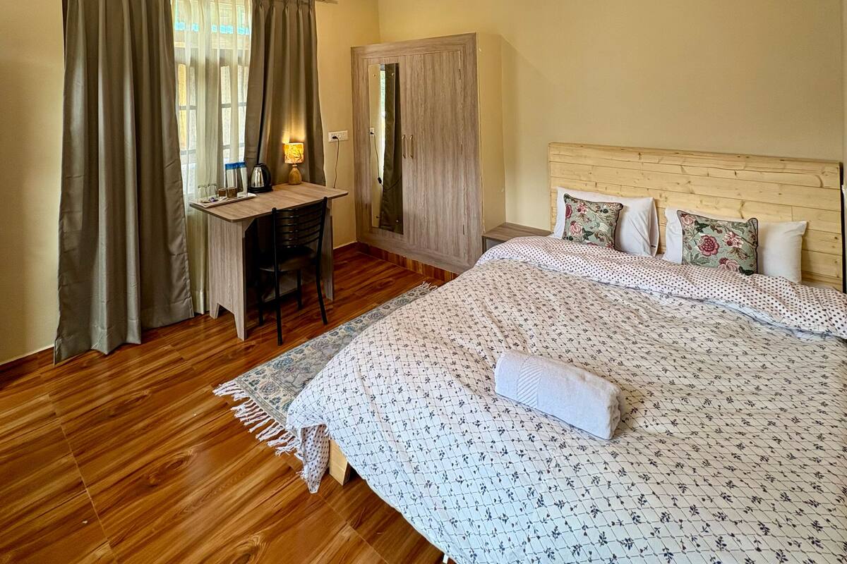Ein Schlafzimmer mit Holzboden, einem Bett mit Blumenmuster-Bettwäsche, einem Schreibtisch mit Stuhl und einem Kleiderschrank.