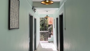 A hallway with a ceiling fan, a framed artwork on the left wall, and a view of a balcony with a railing. - Evolve Dharamkot  (Dharamshala)