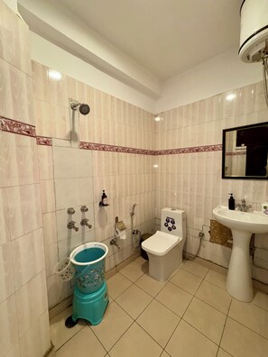 A bathroom with a toilet, bidet, sink, and a blue trash bin. - Evolve Dharamkot  (Dharamshala)