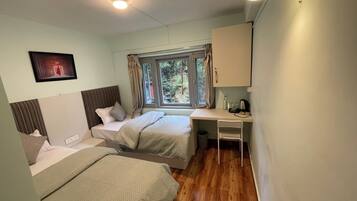 A small, well-lit room with two beds, a desk, and a window with curtains.
