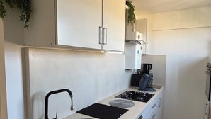 A compact kitchen with white cabinets, a black faucet, and a patterned floor. - La Cachette du Sud  (Vallauris)