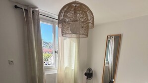A bedroom with a large bed, a ceiling fan, a window with curtains, and a mirror on the wall. - La Cachette du Sud  (Vallauris)