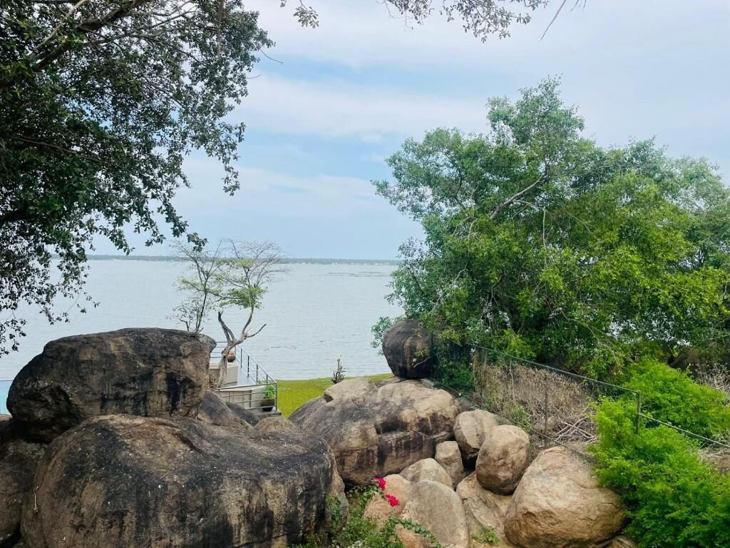 A natural landscape with large rocks, greenery, and a body of water in the background.