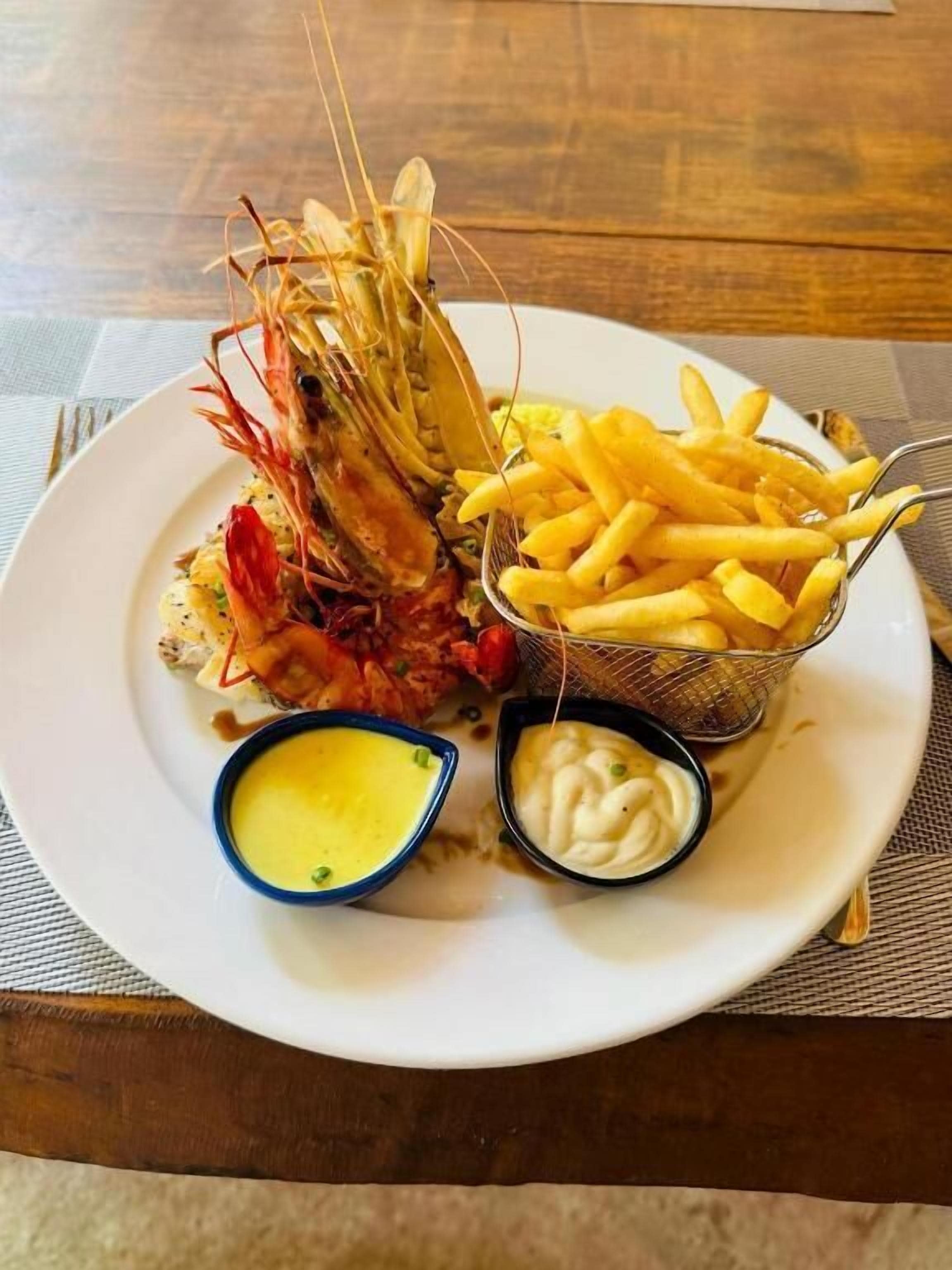A plate with a lobster, fries, and two small containers of sauce.