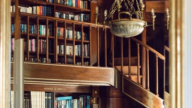 Une bibliothèque avec des étagères en bois, un lustre et un escalier.