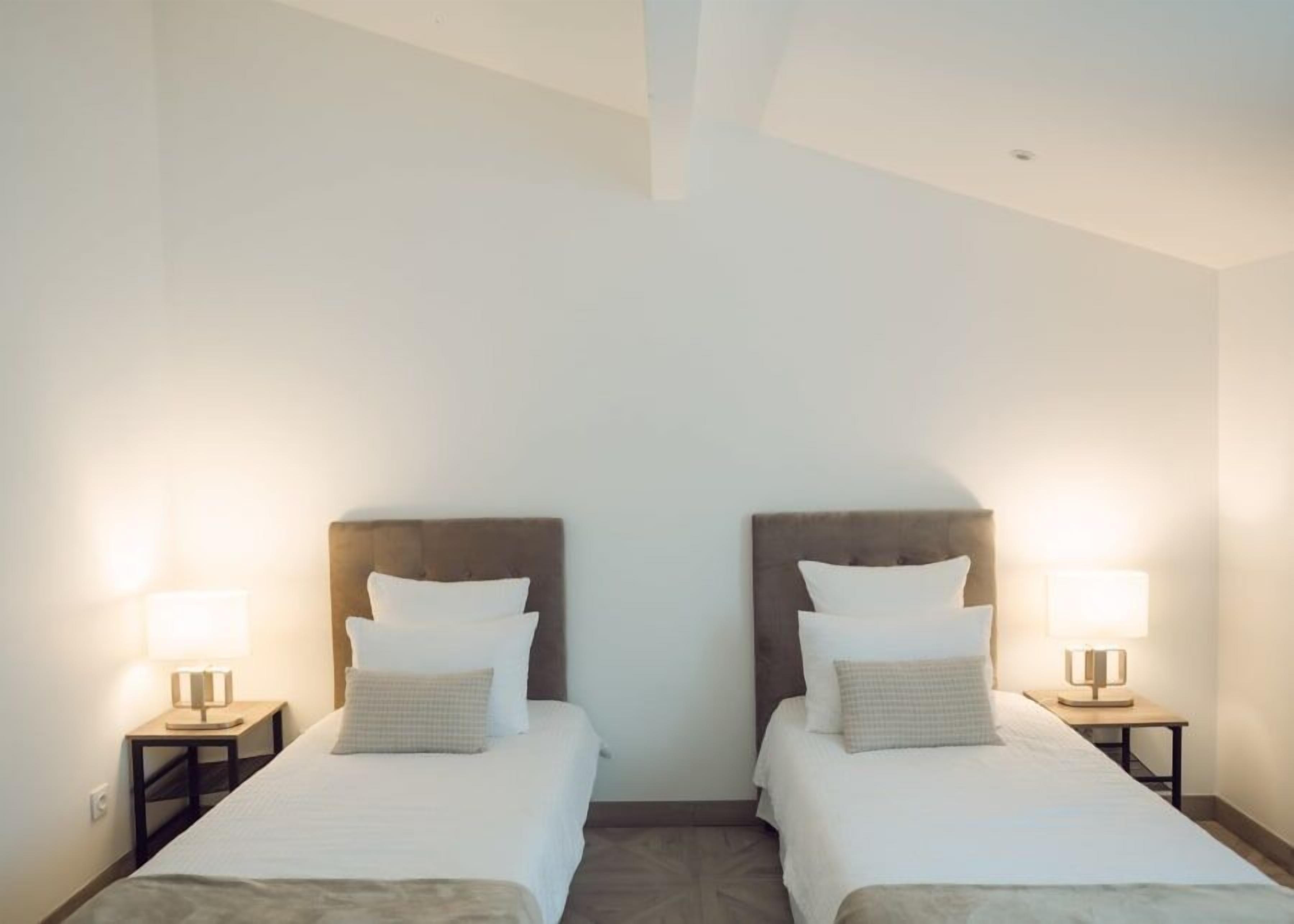 A hotel room with two single beds, each with a headboard, a bedside table, and a lamp.