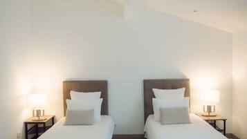 A hotel room with two single beds, each with a headboard, a bedside table, and a lamp.