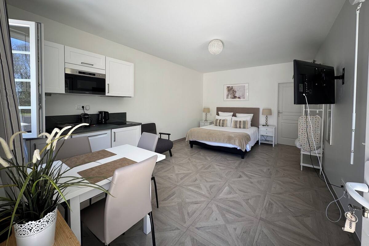 A compact hotel room with a kitchenette, a bed, a TV, and a dining area with a table and chairs.