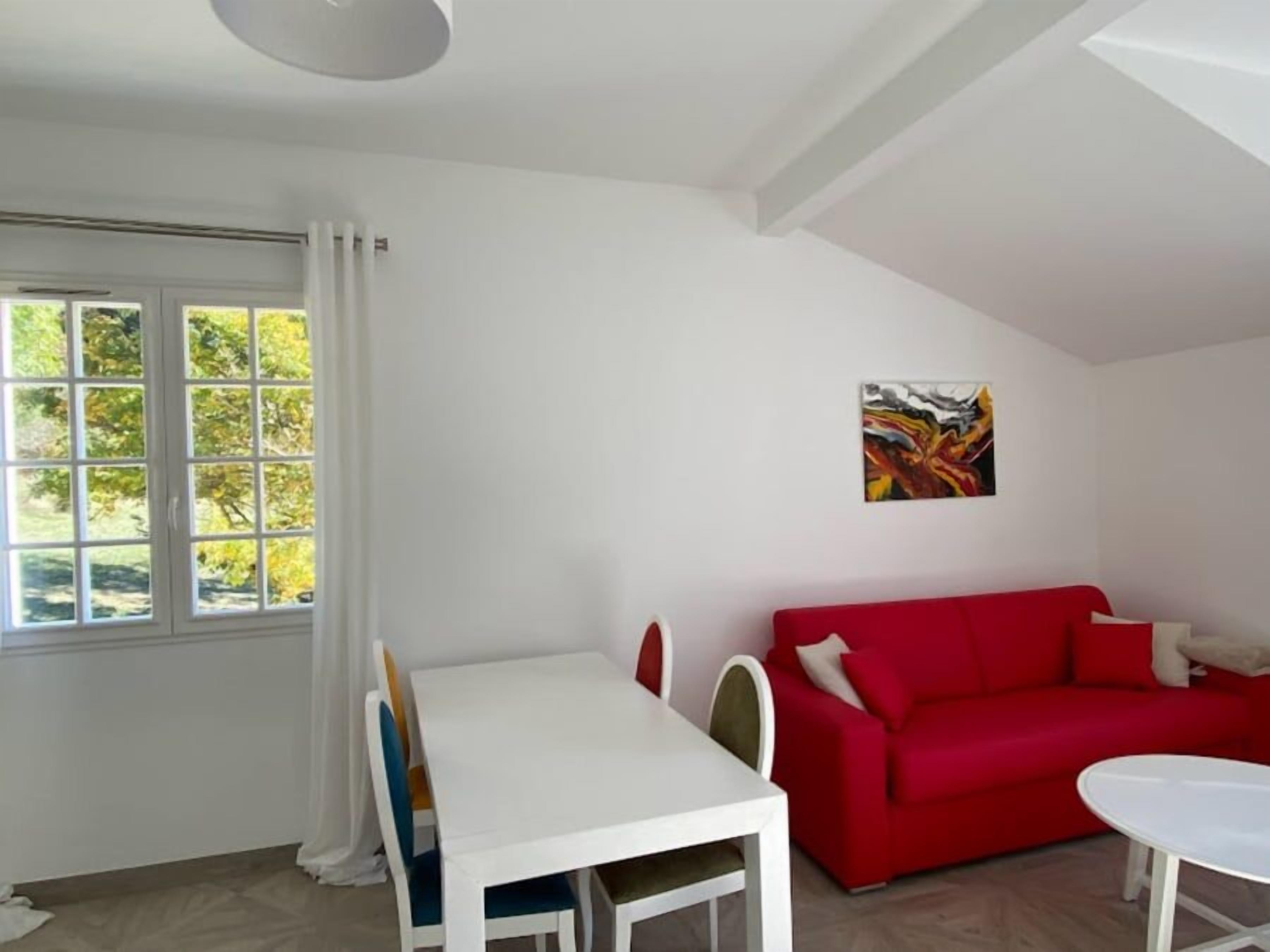 Una habitación con una mesa y sillas blancas, un sofá rojo y un cuadro en la pared.