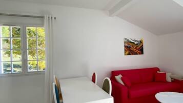 Una habitación con una mesa y sillas blancas, un sofá rojo y un cuadro en la pared.