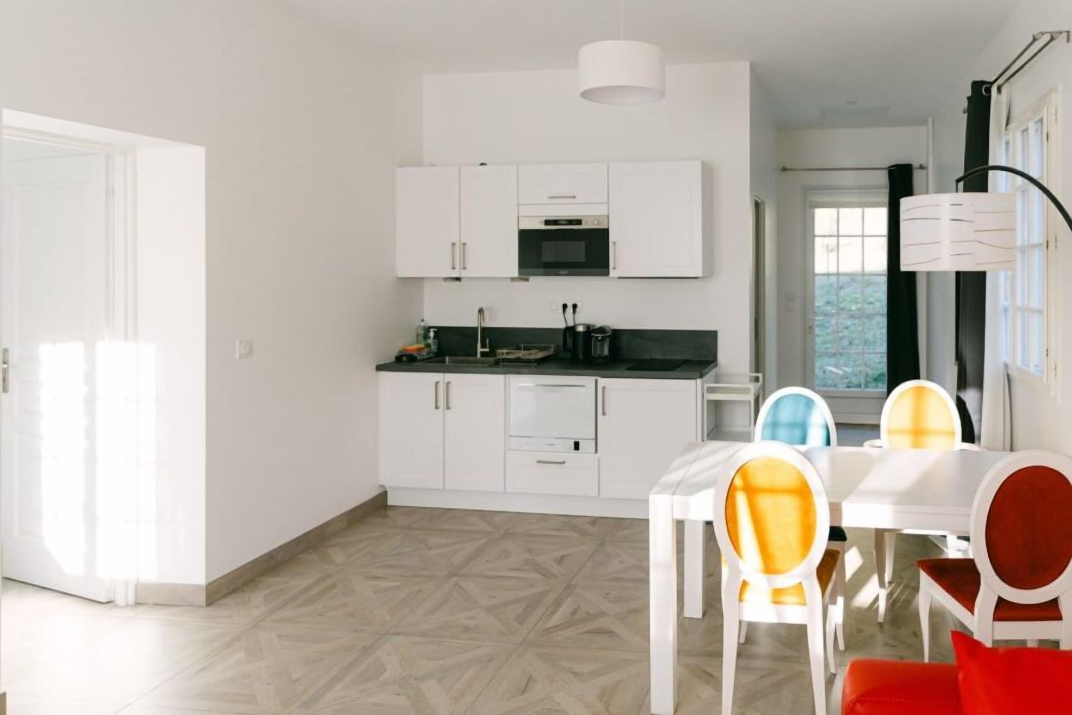 A modern kitchen with white cabinets, a black countertop, and a dining area with a white table and colorful chairs.