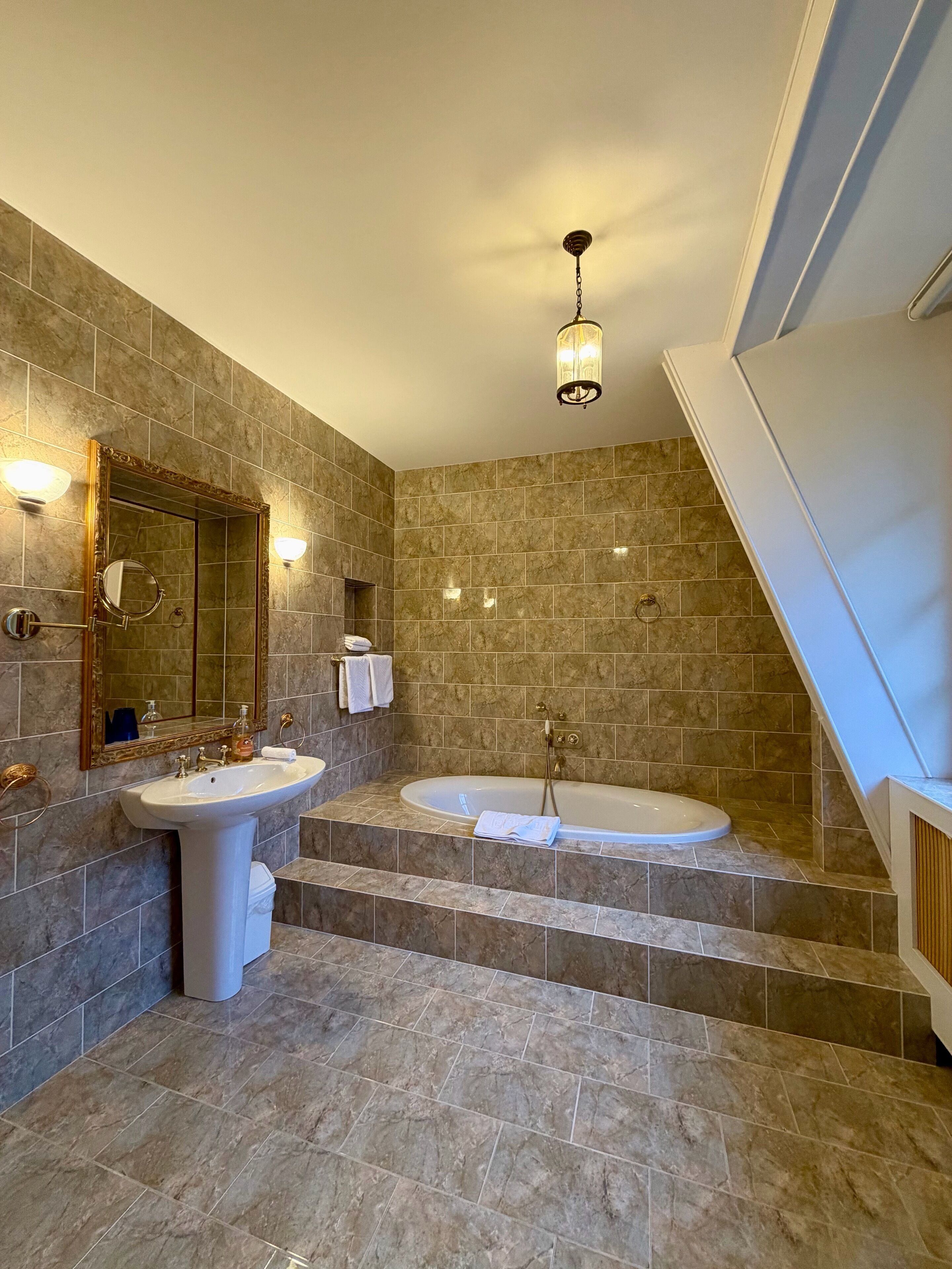 Un baño con dos lavamanos, un espejo grande, una bañera y un candelabro.