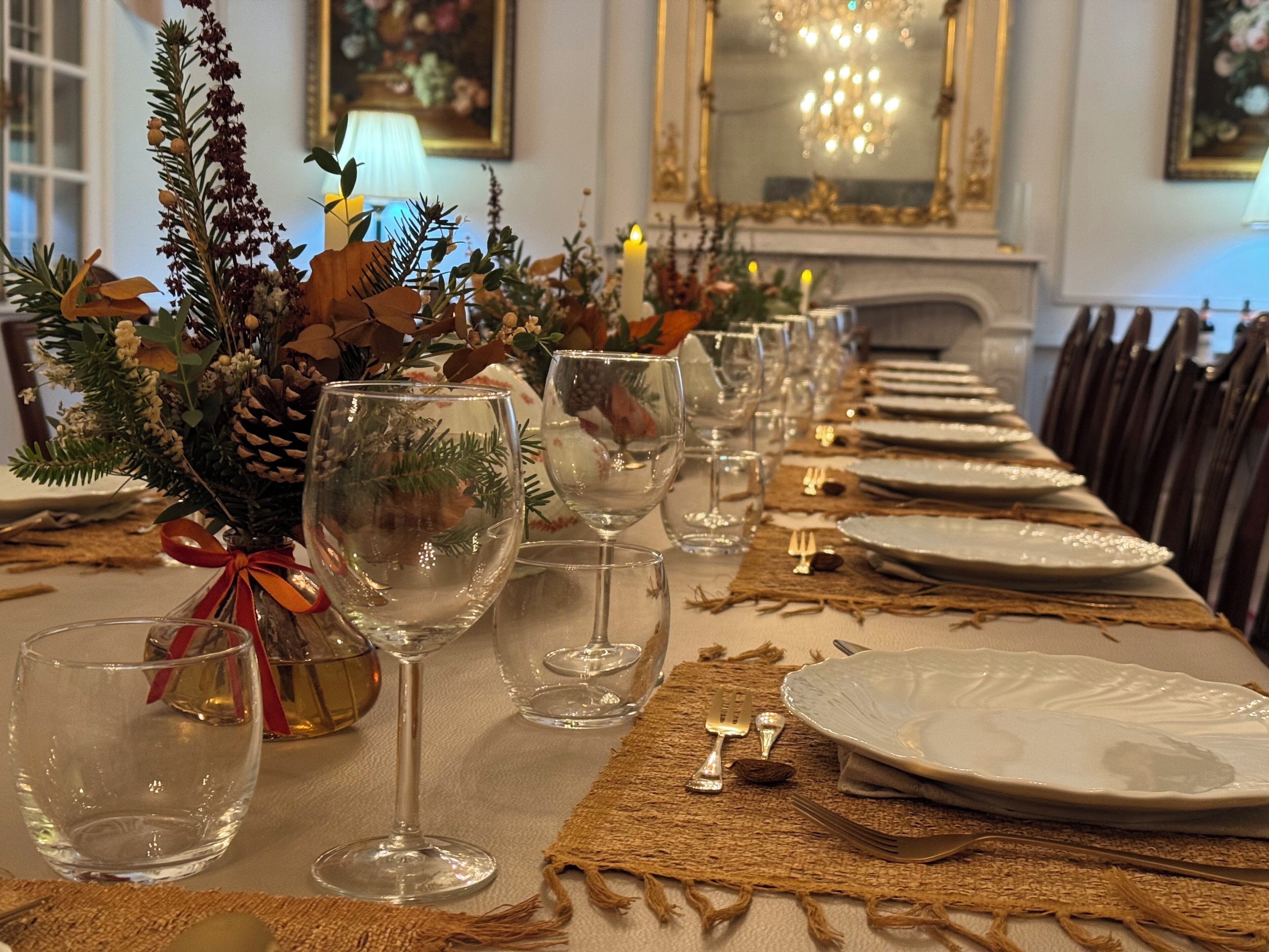 Mesa de comedor formal dispuesta con copas de vino, platos y cubiertos, decorada con adornos de temporada y un centro de mesa.