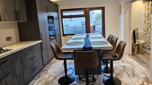 Una cocina moderna con armarios de madera oscura, encimera de mármol y comedor con una mesa grande y sillas.