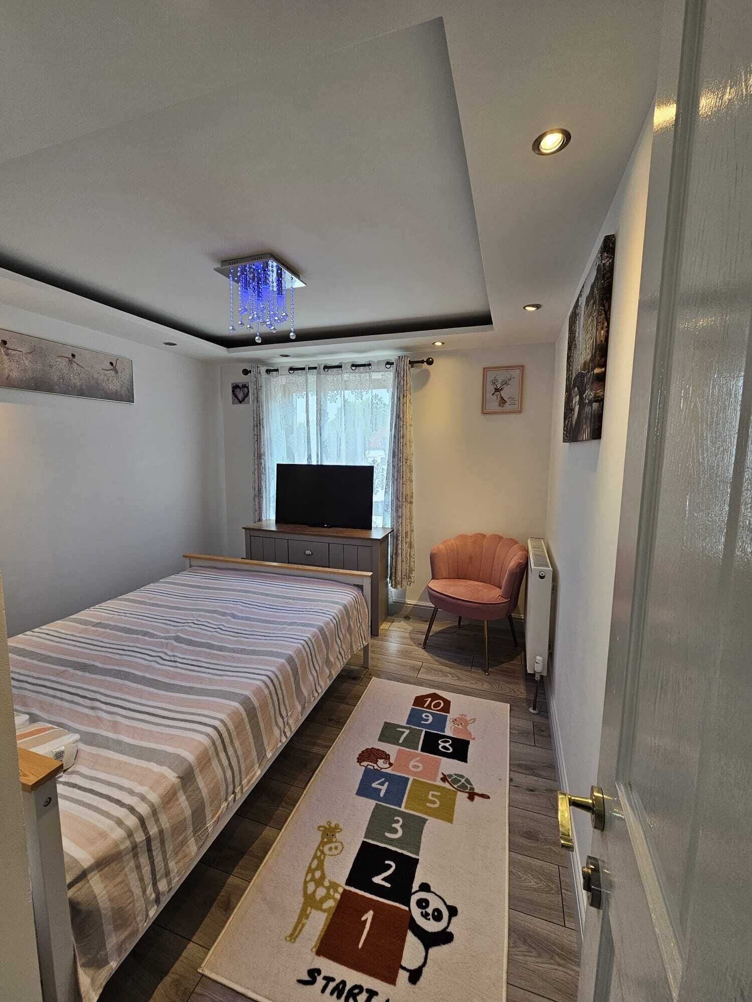 Ein Schlafzimmer mit Bett, Fernseher, Stuhl und Teppich mit einem Hütchenspiel.