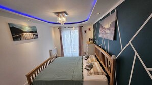 Un dormitorio con cama, mesita de noche, ventana con cortinas y decoración en la pared.