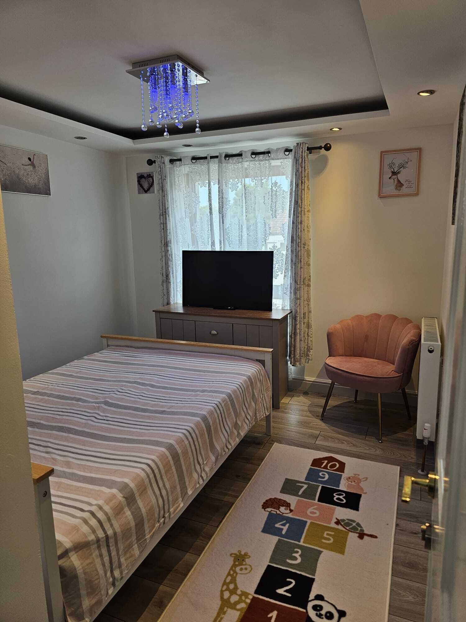 Un dormitorio con una cama, un televisor sobre un soporte, una silla y una alfombra con números e ilustraciones de animales.