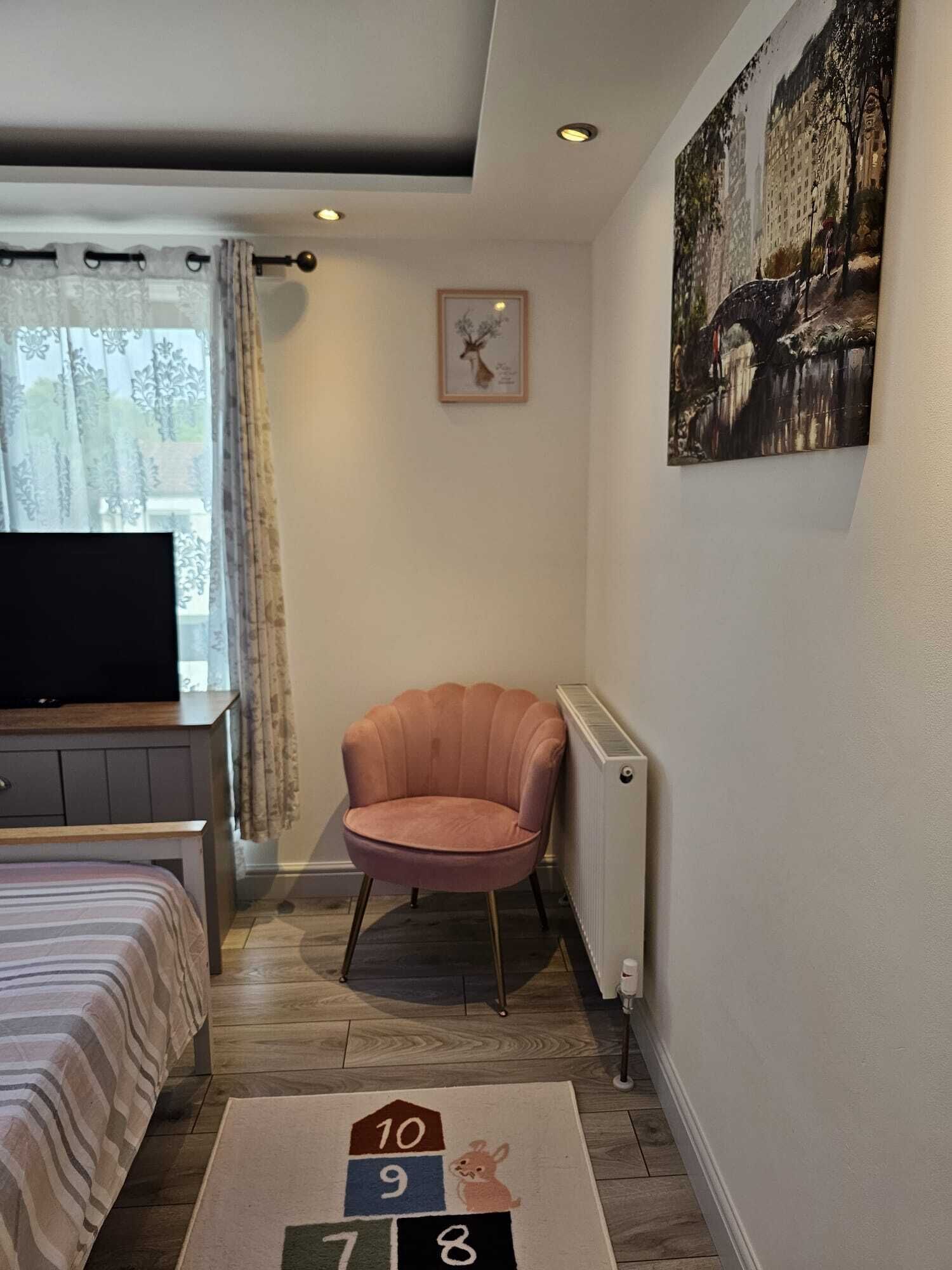 A bedroom with a bed, a TV, a pink chair, a radiator, and a rug with numbers.