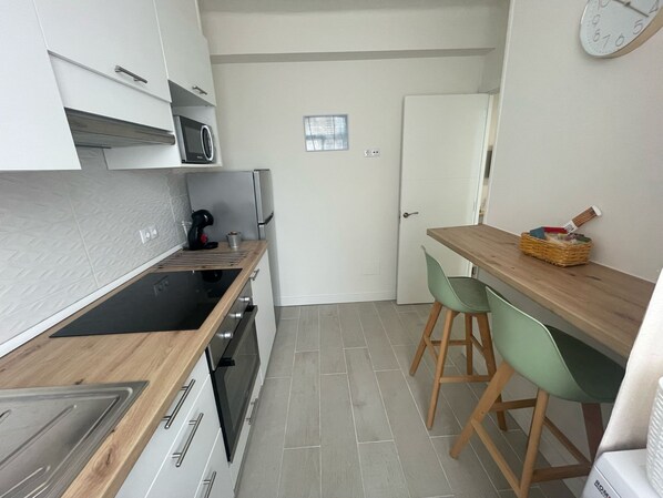 Una cucina compatta con forno a microonde, piano cottura e un piccolo angolo ristoro con sedie.