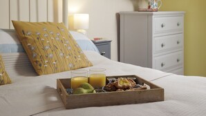 Un letto rifatto con cura, un cuscino a motivi floreali, un comodino con una lampada e un vassoio con prodotti per la colazione.