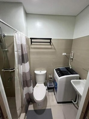 A compact bathroom with a toilet, a shower, a sink, and a small washing machine.