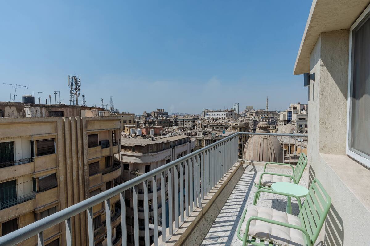 Un balcone con vista su una zona urbana densamente popolata, caratterizzata da numerosi edifici e un cielo sereno.