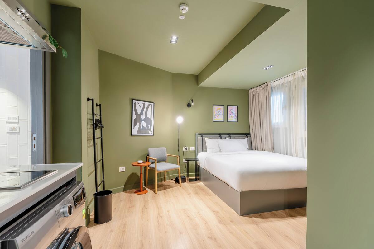 Camera d'albergo con un letto, una poltrona, un tavolino, una lavatrice e una TV a parete.