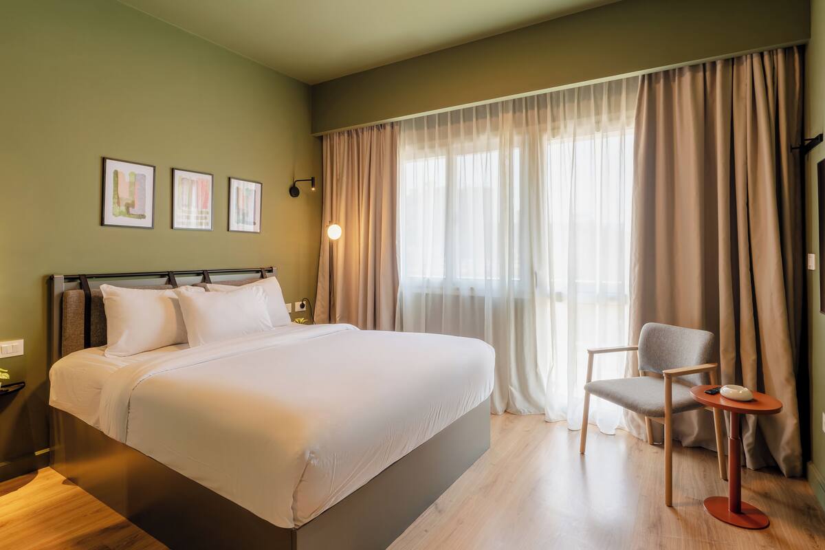 Una camera d'albergo con un letto grande, una sedia, un tavolino e una finestra con tende.