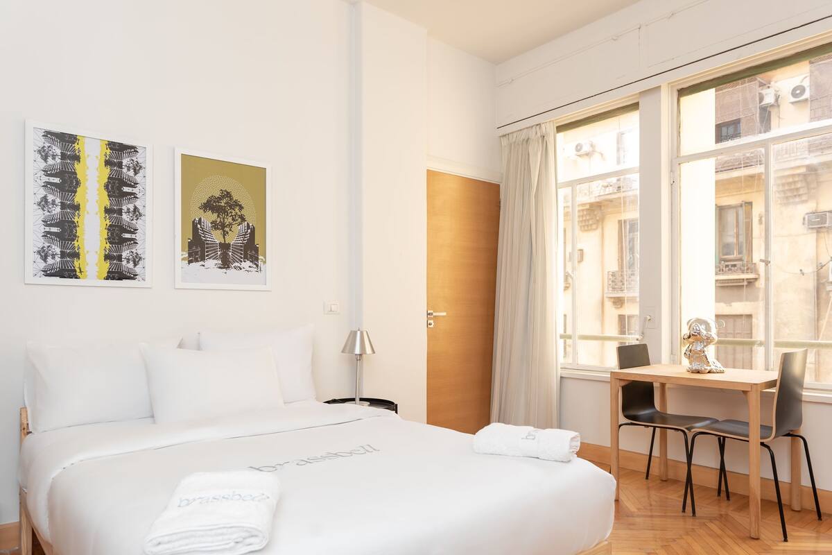 Camera d'albergo con un letto grande, una scrivania e una finestra vista edifici.