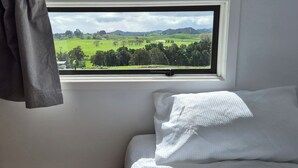 A bedroom with a window view of a green landscape, a white pillow, and a gray curtain.