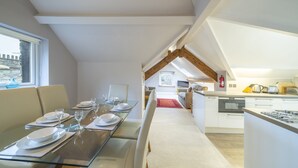 A modern dining area with a glass table set for four, a kitchen with white cabinets, and a view of the outside. - The Viewpoint -  Central Ambleside and short stroll to shops, cafes (Ambleside)