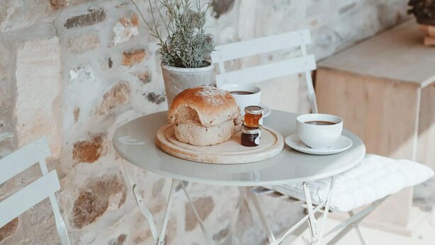 Une table en métal blanc sur laquelle se trouvent un petit pain, une tasse de café et une petite plante en pot.