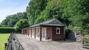 Une étable dotée d’un toit en pierre et de murs en bois, entourée d’un chemin de gravier et d’une clôture en bois.