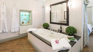 Une salle de bain avec une grande baignoire, un miroir et deux plantes en pot.