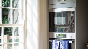 A kitchen with a window, a trash can, and a microwave.