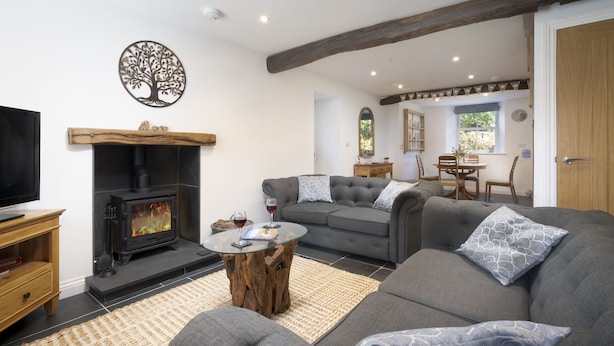 A living room with a fireplace, grey sofas, a coffee table, and a TV. - Cringlemire Farm Cottage -  17th century cottage that sleeps 4 guests  in 2 bedrooms (Bouth)