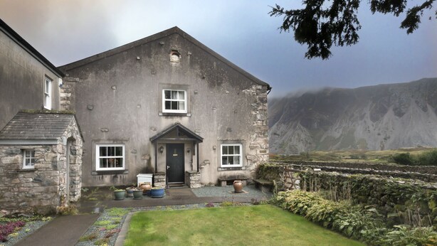 A stone building with a front door, windows, and a small porch area with potted plants.