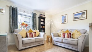 A living room with two sofas, a bookshelf, and a window with curtains.