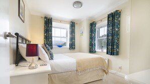 A bedroom with a bed, a bedside table with a lamp, a window with curtains, and a view of the outdoors.