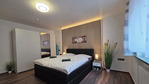 Ein modernes Schlafzimmer mit einem großen Bett, einem Kleiderschrank, einem Nachttisch mit Lampe und einem an der Wand befestigten Regal.