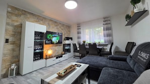 Ein modernes Wohnzimmer mit Flachbildfernseher, einer Couch, einem Couchtisch und einem Essbereich mit Tisch und Stühlen.